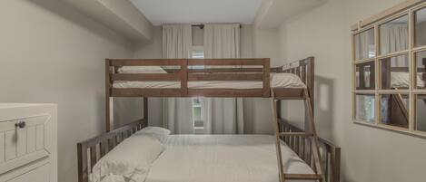 Una cama individual superpuesta en una habitación con un aparador, una ventana con cortinas y un espejo en la pared.