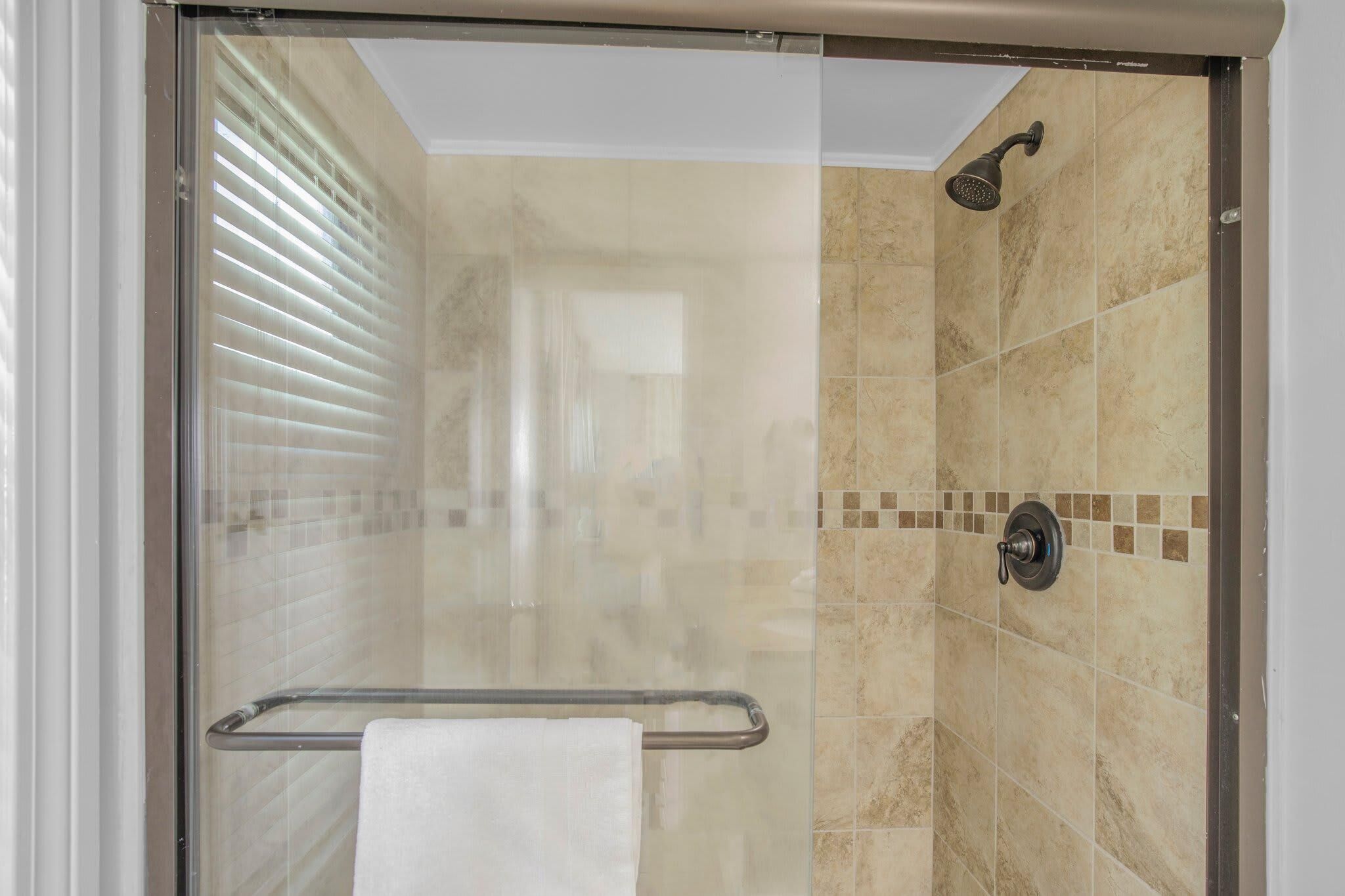 A glass-enclosed shower area with a handheld showerhead, a towel rack, and a tiled wall.