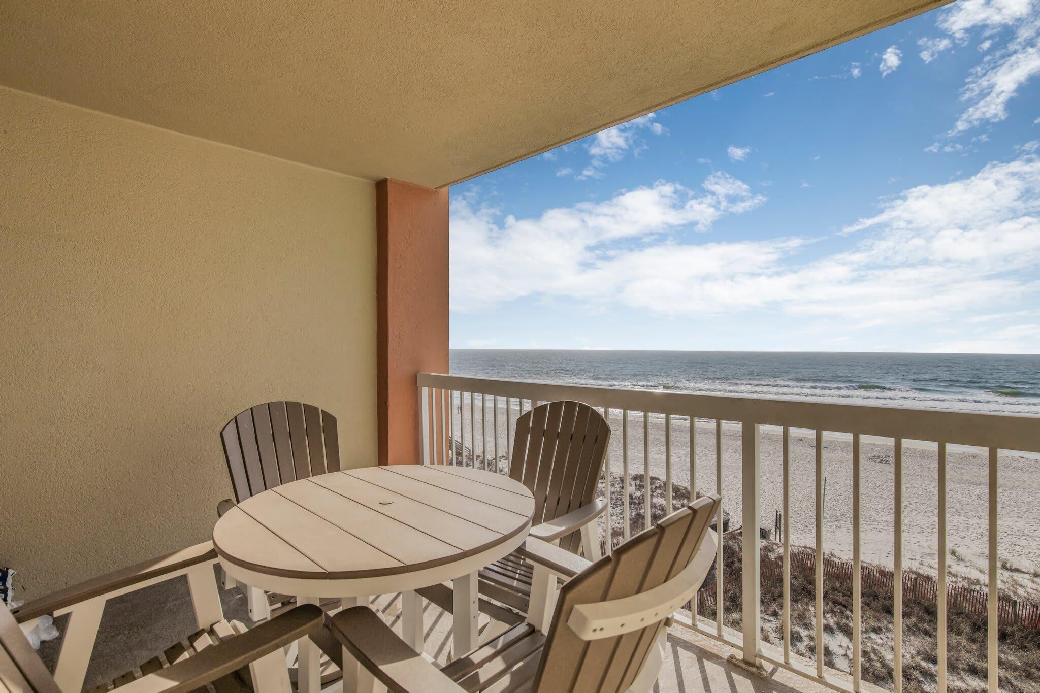 A balcony with a table and chairs, overlooking a beach.