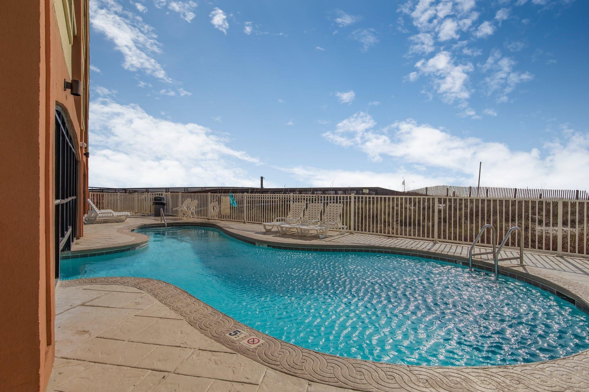 A swimming pool with lounge chairs and a fence, surrounded by a building.
