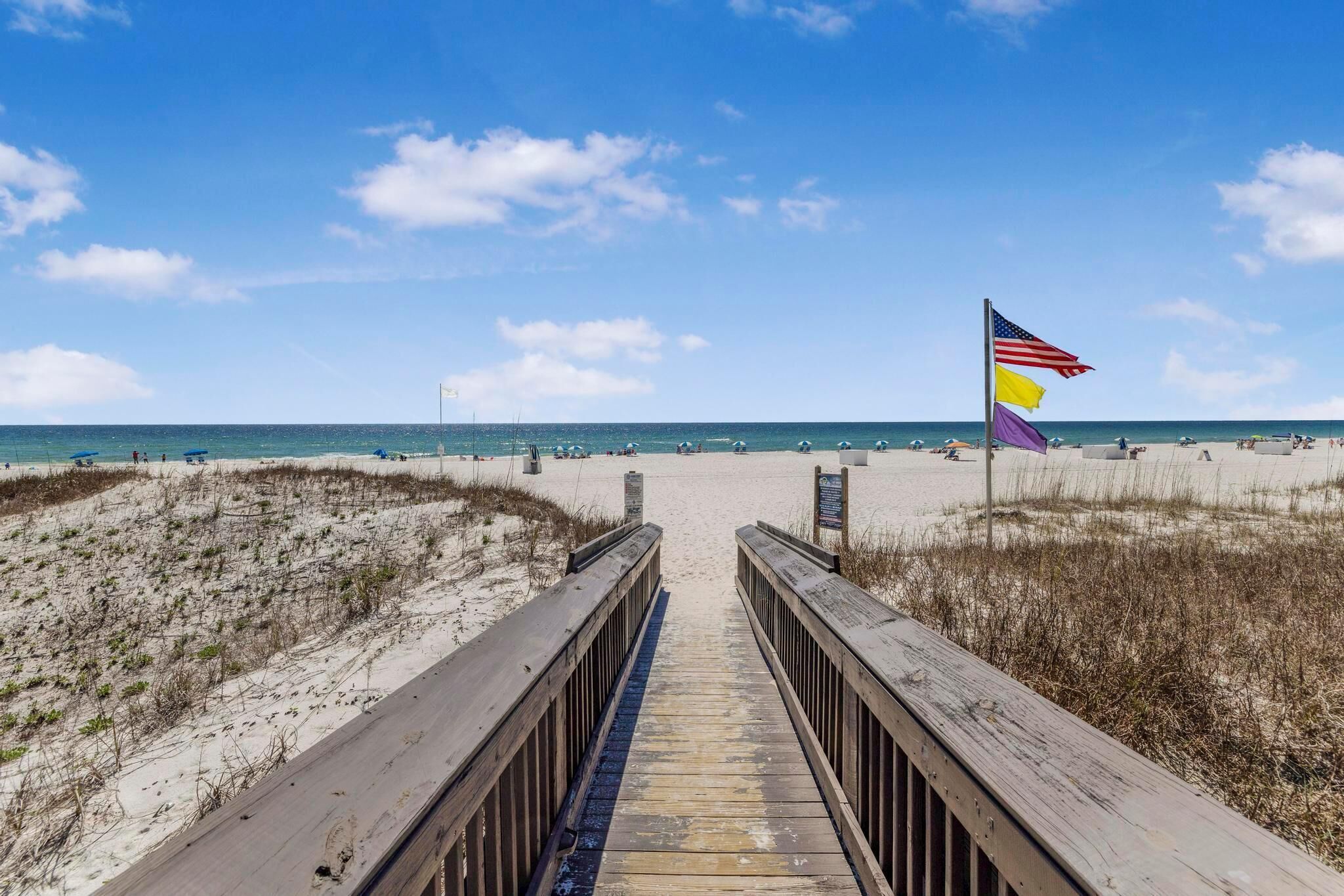 A wooden boardwalk leading to a beach with a flag.