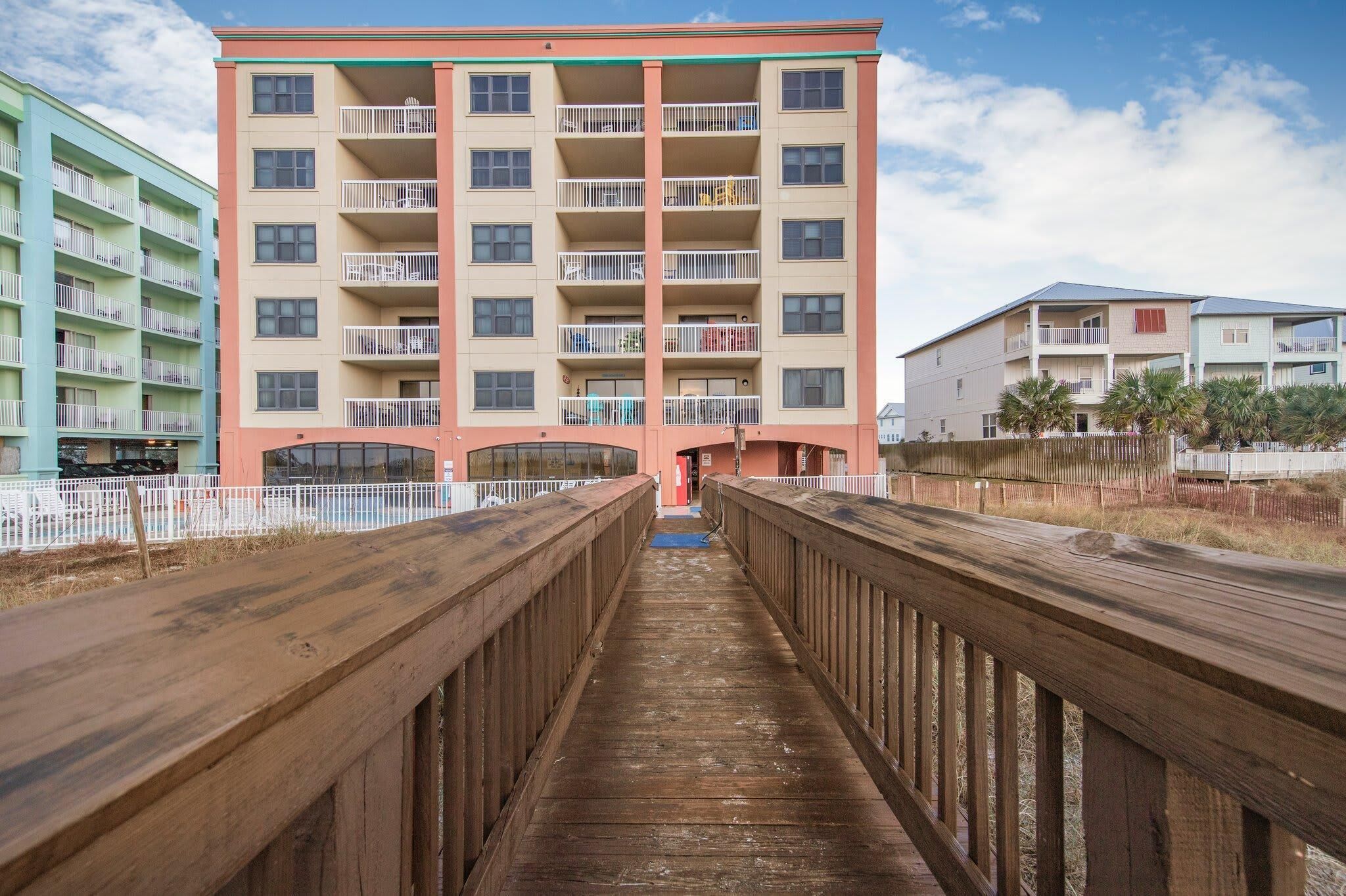 A multi-story hotel with balconies, a wooden walkway, and a clear sky.
