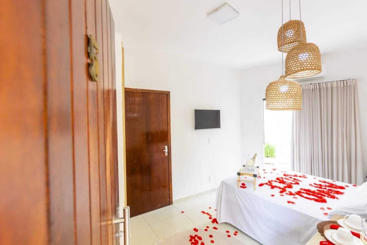 Habitación de hotel con una cama cubierta de pétalos de rosa, un armario de madera, un televisor de pantalla plana y una lámpara en el techo.