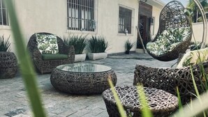 Un patio al aire libre con mobiliario de mimbre, plantas en macetas y un cielo despejado.