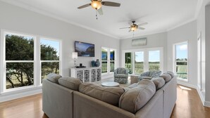 A spacious living room with a large sectional sofa, two ceiling fans, and large windows offering a view of the outdoors. - Lotsa Sand C (Gulf Shores)