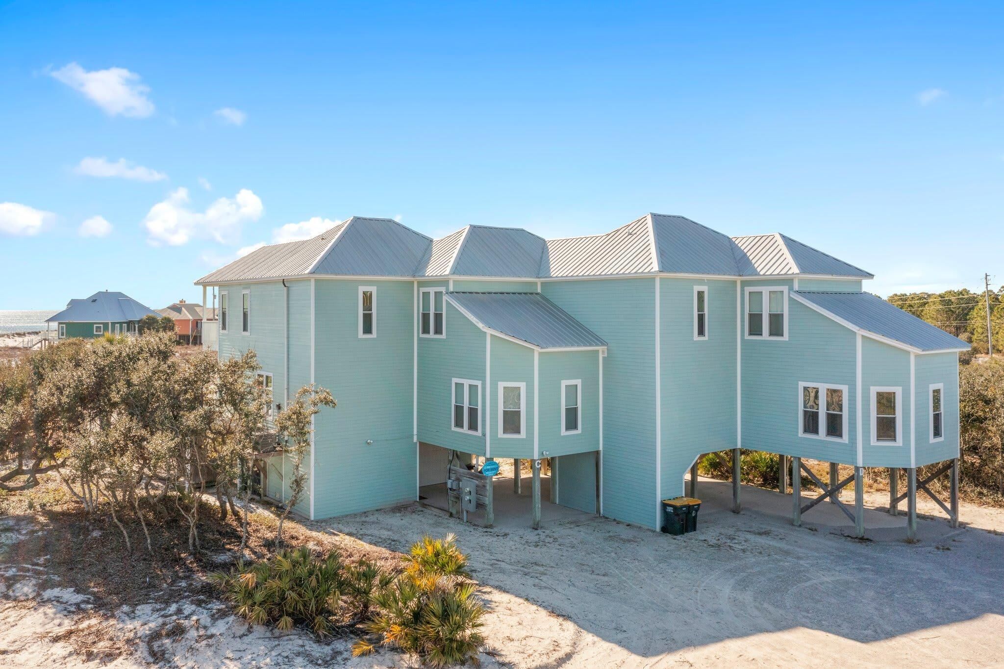 A light blue two-story house with a gabled roof, a covered porch, and a sandy ground.