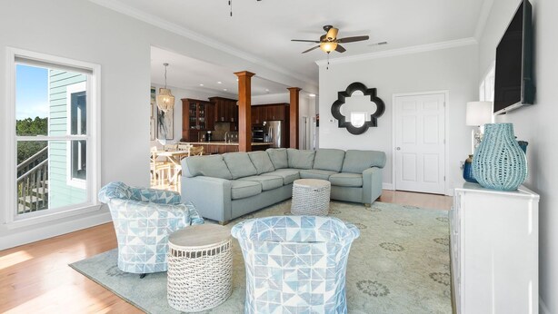 A spacious living room with a large sectional sofa, two patterned armchairs, and a coffee table. There are ceiling fans, a TV mounted on the wall, and a kitchen area visible through an open door. - Lotsa Sand C (Gulf Shores)