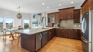 A modern kitchen with wooden cabinets, a large island, and a view of the outdoors. - Lotsa Sand C (Gulf Shores)