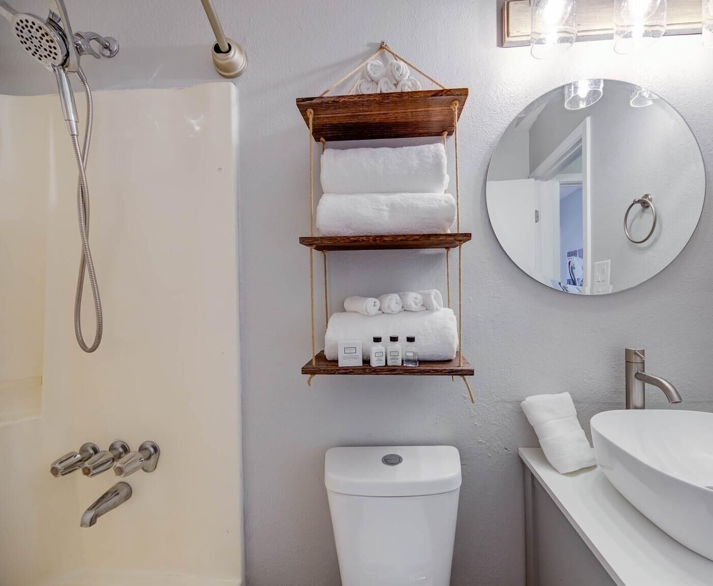 Une salle de bain avec douche, toilettes et lavabo. On y trouve des étagères en bois où sont rangées des serviettes et des articles de toilette.