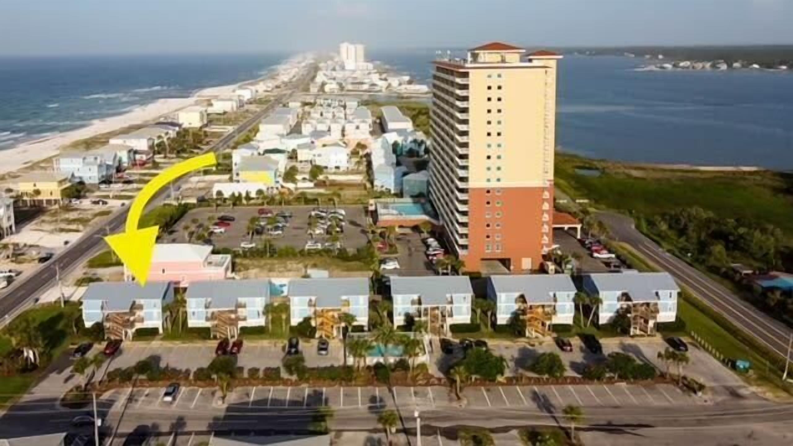 Vue aérienne d’un hôtel situé sur la côte, composé de plusieurs bâtiments, avec un parking et une vue sur l’océan.