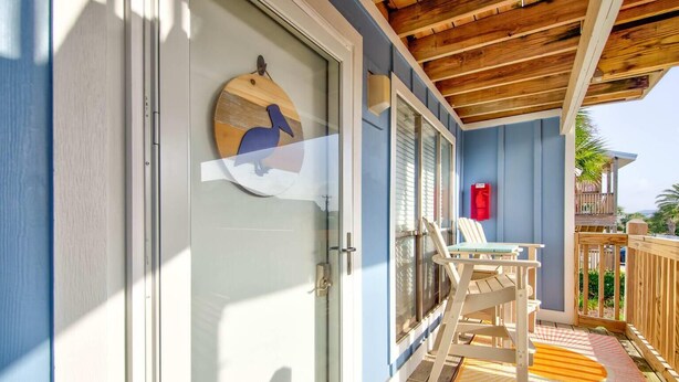 Un espacio exterior techado con cubierta de madera, una puerta de vidrio con una obra de arte de madera, y un extintor rojo en la pared.