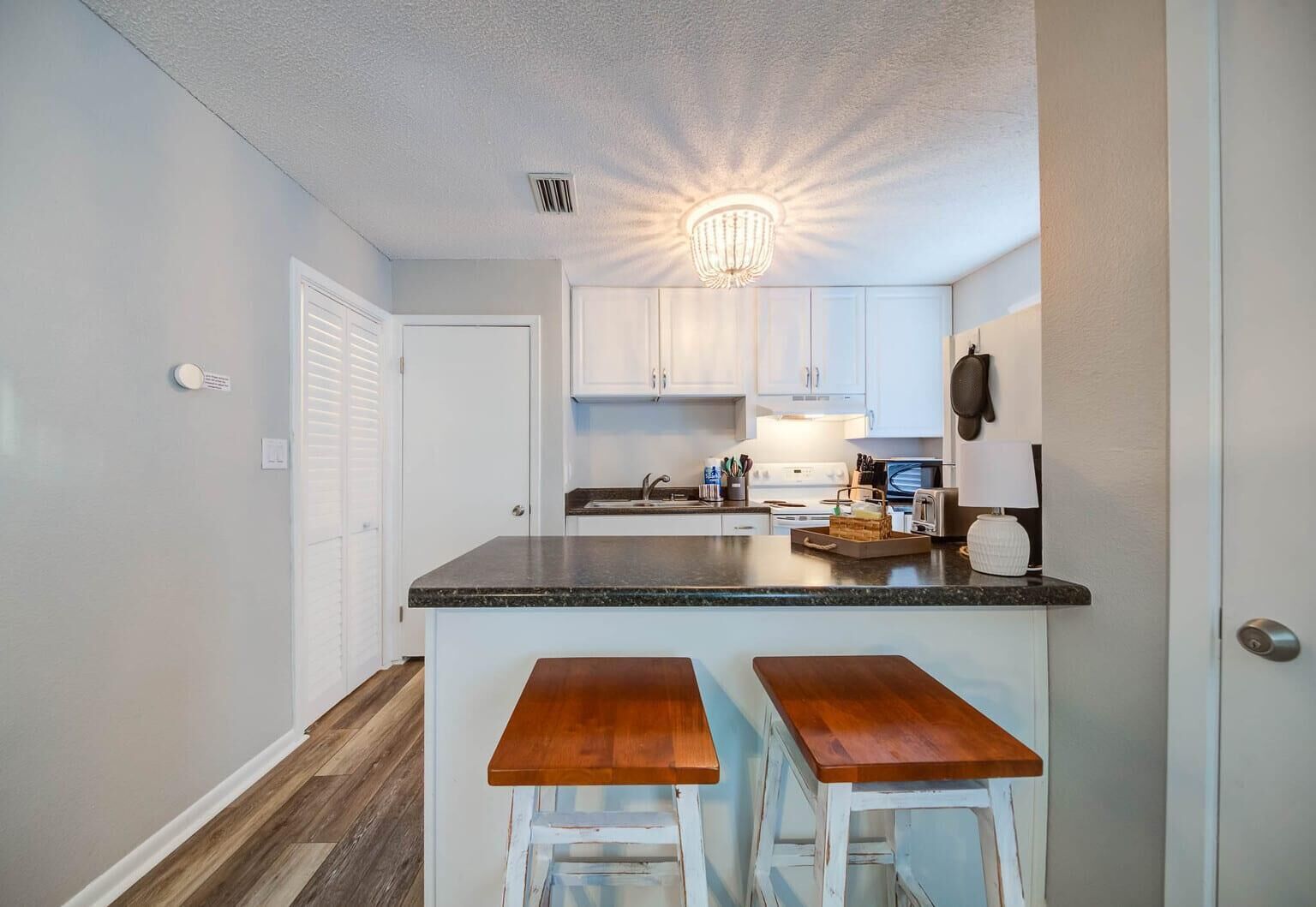 A compact kitchen with white cabinets, a granite countertop, and two wooden bar stools.