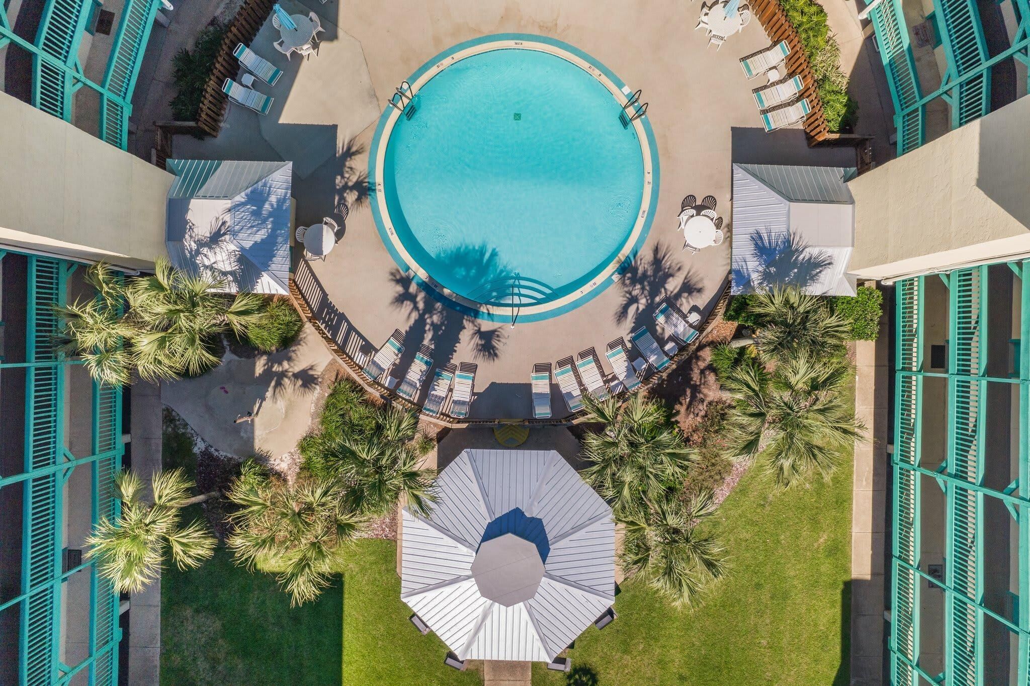An aerial view of a pool area with a circular pool, surrounded by lounge chairs and palm trees.