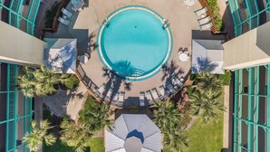 Vue aérienne d’un espace piscine avec une piscine circulaire, entourée de chaises longues et de palmiers.