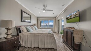 A bedroom with a bed, a nightstand, a dresser, a ceiling fan, a TV, and a window with a view of the ocean. - Marlin Key 4C (Orange Beach)