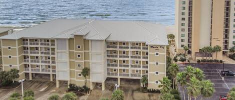 A multi-story hotel with a flat roof, multiple balconies, and a parking area with palm trees.