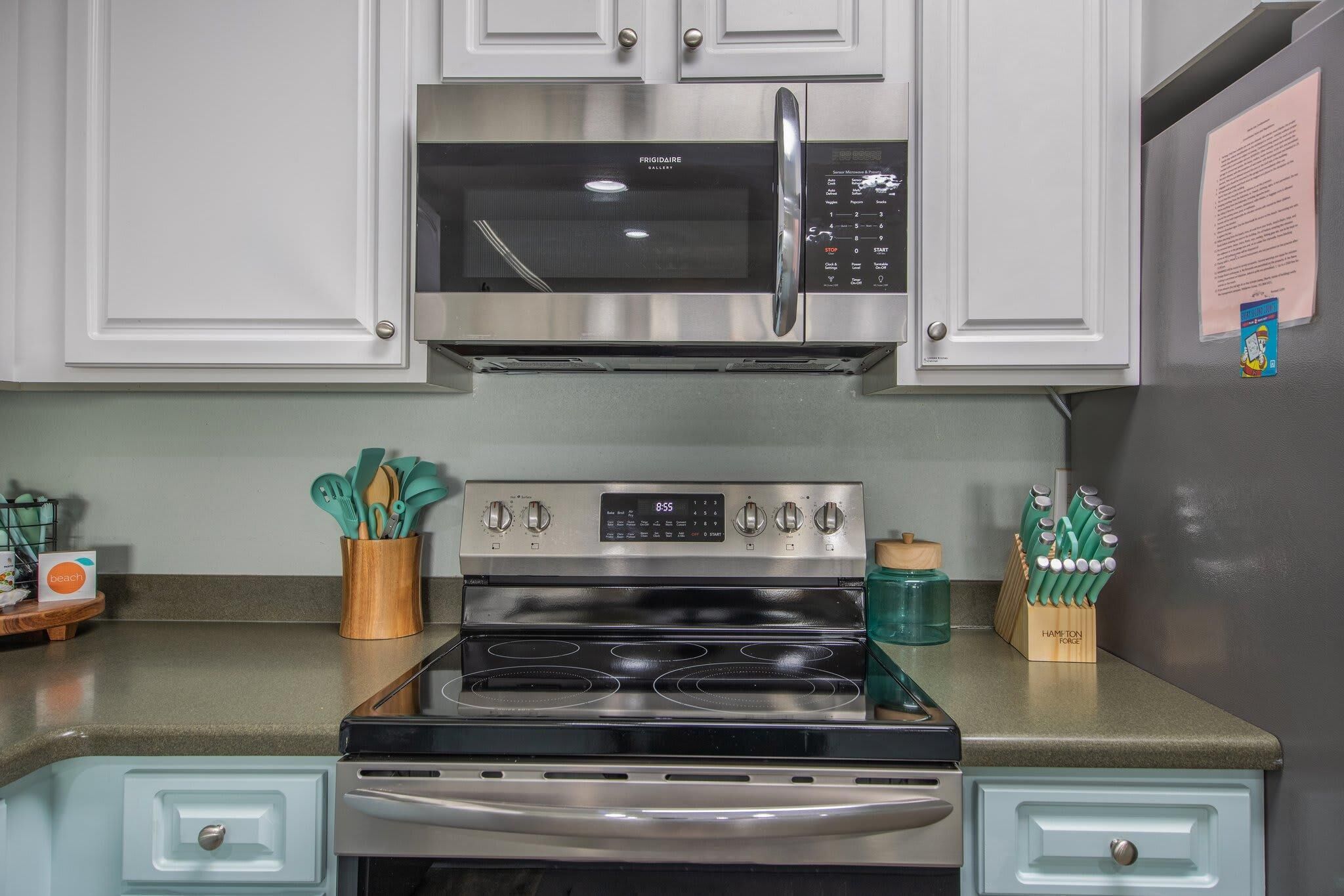 A kitchen with a stainless steel microwave, oven, and gas range. There are cabinets above and below the appliances, and a small wooden tray with utensils on the counter.