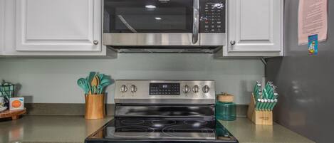 A kitchen with a stainless steel microwave, oven, and gas range. There are cabinets above and below the appliances, and a small wooden tray with utensils on the counter.