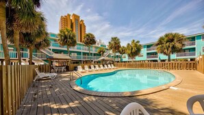 A pool area with a wooden deck, lounge chairs, and a clear blue pool. - Lani Kai 103 (Gulf Shores)