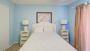 A bedroom with a single bed, two bedside tables with lamps, a ceiling fan, and a painting on the wall. - Lani Kai 103 (Gulf Shores)