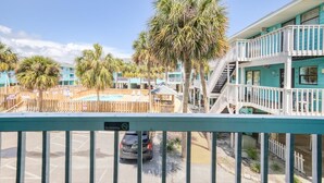 A view of a motel with a pool, palm trees, and a fenced area. - Lani Kai 103 (Gulf Shores)