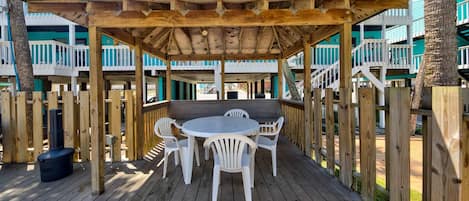 A wooden deck with a covered patio area, white plastic chairs, and a round table.