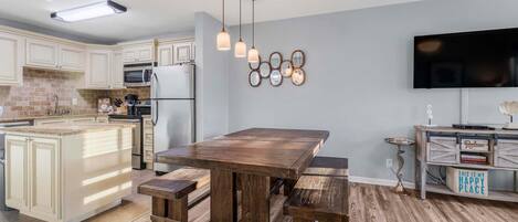 A modern kitchen with a central island, wooden dining table, and pendant lighting.