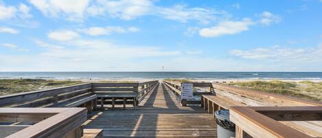 A wooden boardwalk leading to a beach with a clear sky.