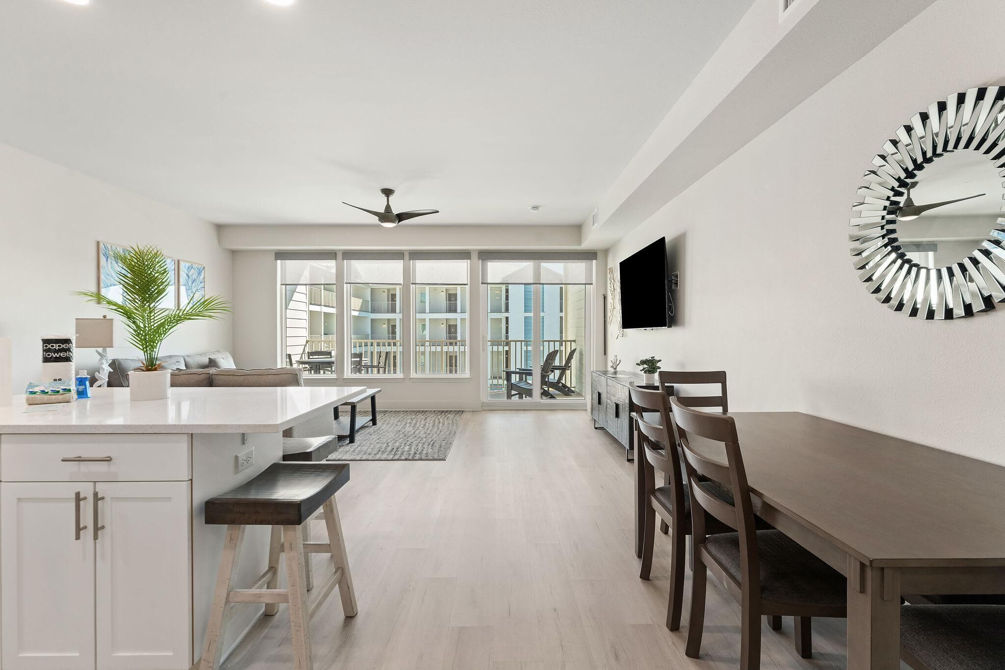 A modern kitchen with a central island, a dining area with a long table and chairs, and a large window providing a view of the city.