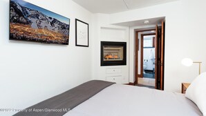 Une chambre à coucher comprenant un lit, une cheminée, un téléviseur et une porte donnant sur une salle de bain.
