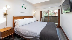 Une chambre dotée d’un grand lit, de lampes de chevet, d’un téléviseur à écran plat et d’une fenêtre donnant sur un paysage verdoyant.
