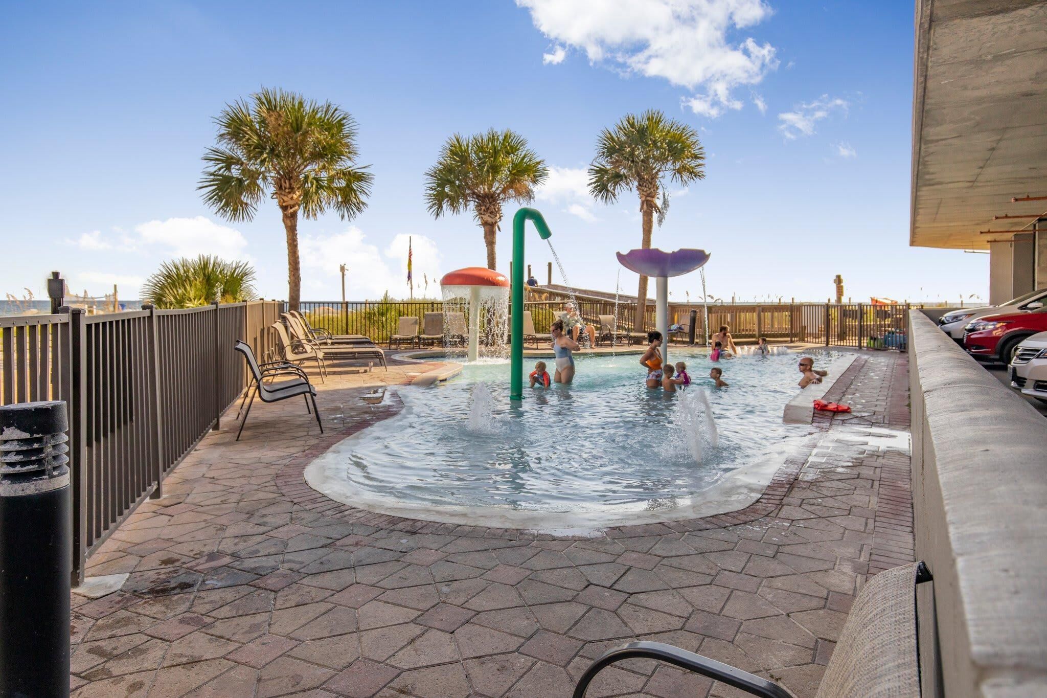A swimming pool area with palm trees, lounge chairs, and a water fountain.