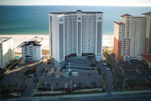 A high-rise hotel with multiple floors, a parking lot, and a beach view. - Seawind 1609 (Gulf Shores)