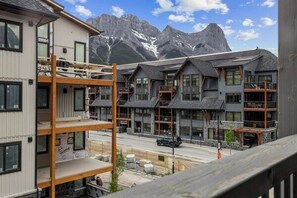 A multi-story building with balconies, a street in front, and mountains in the background.