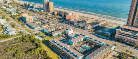 A coastal cityscape with a beachfront hotel, high-rise buildings, and a clear view of the ocean.