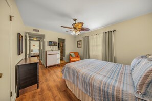 Un dormitorio con una cama, un escritorio, una silla, un ventilador de techo y una puerta que da a otra habitación.