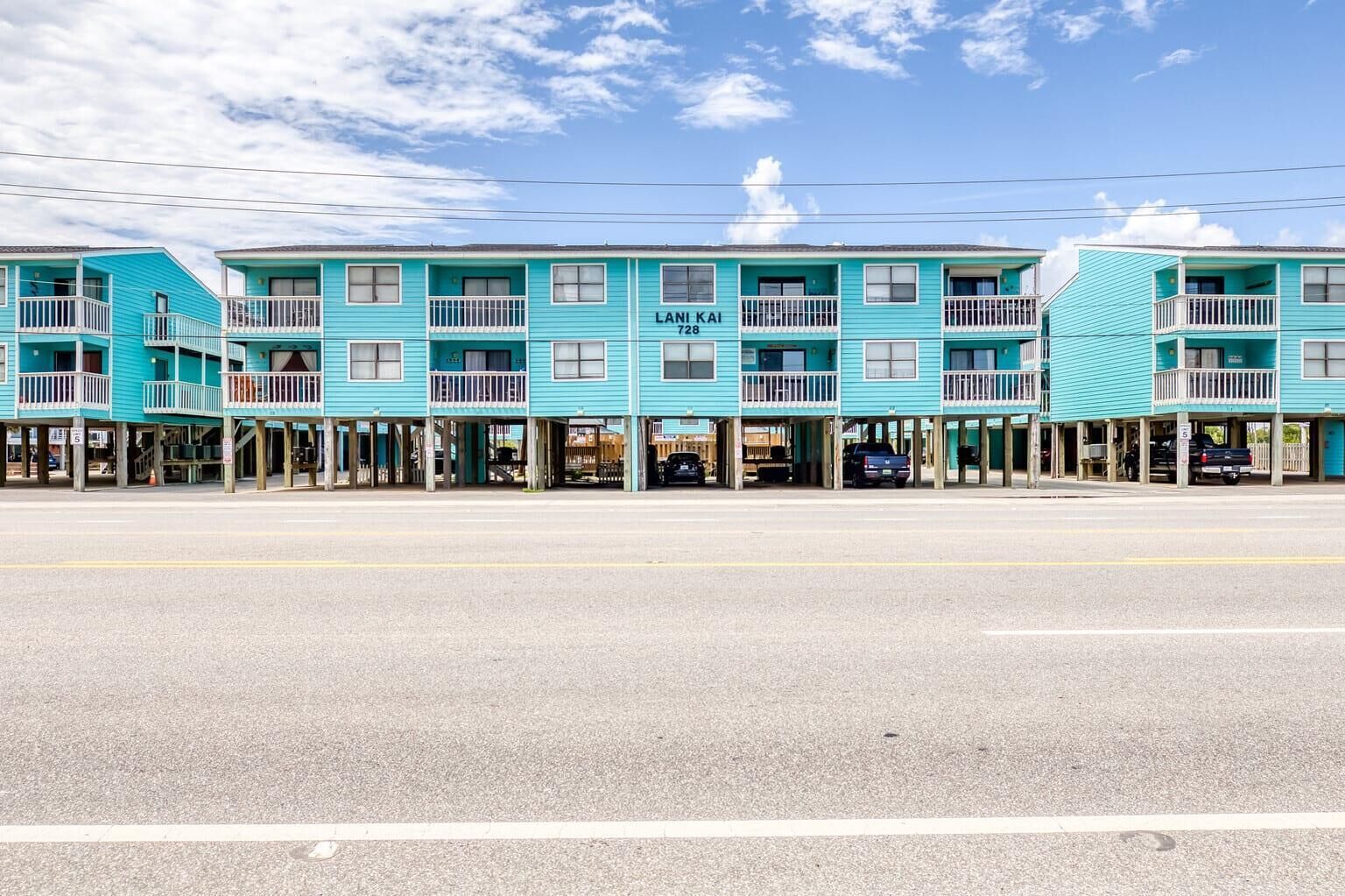 Een rij turquoise motelgebouwen met balkons, een heldere lucht en een weg op de voorgrond.