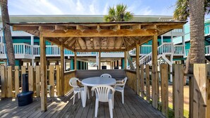 Une terrasse en bois avec un espace patio couvert, des chaises en plastique blanches et une table ronde.