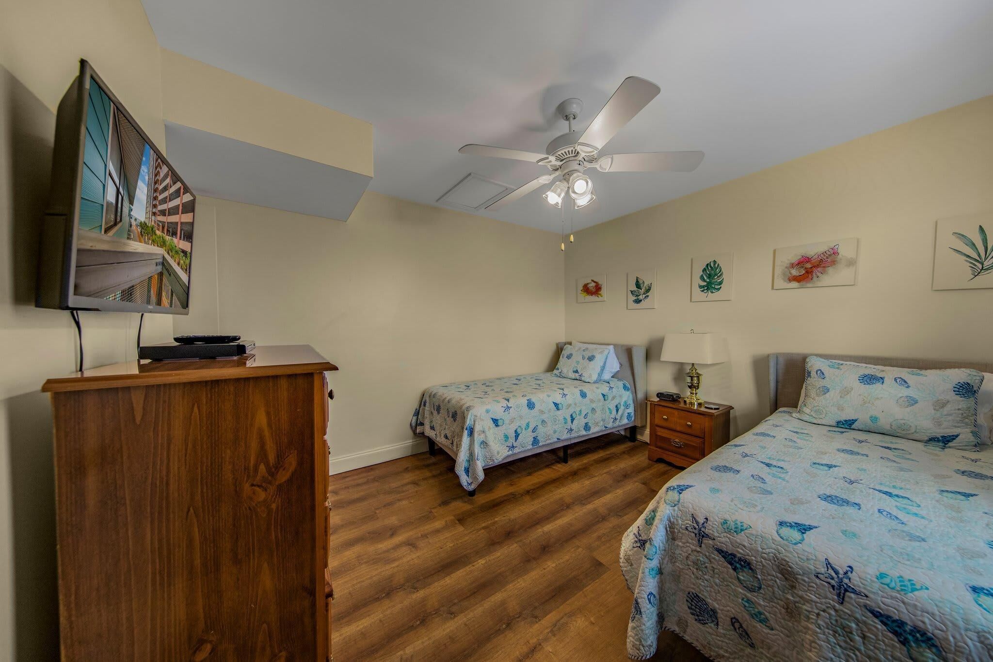Une chambre avec deux lits, un ventilateur de plafond et une commode en bois.