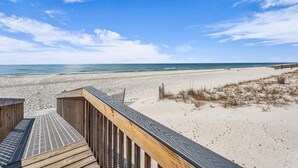Ein hölzerner Steg führt zu einem Sandstrand mit freiem Blick auf den Ozean.