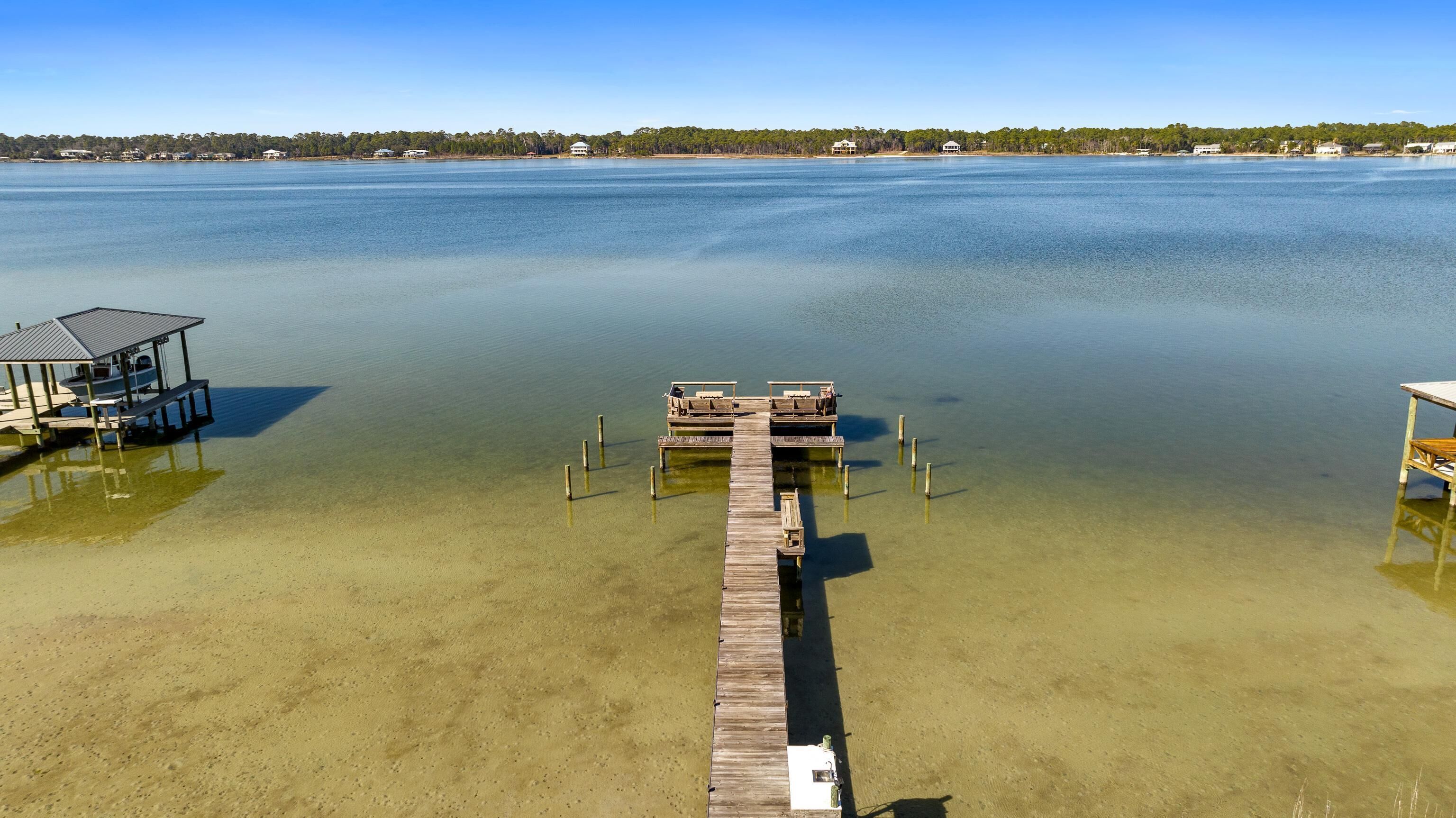 Une jetée en bois s’étendant dans une étendue d’eau calme, avec un petit quai et un espace aménagé avec des sièges sur la gauche.