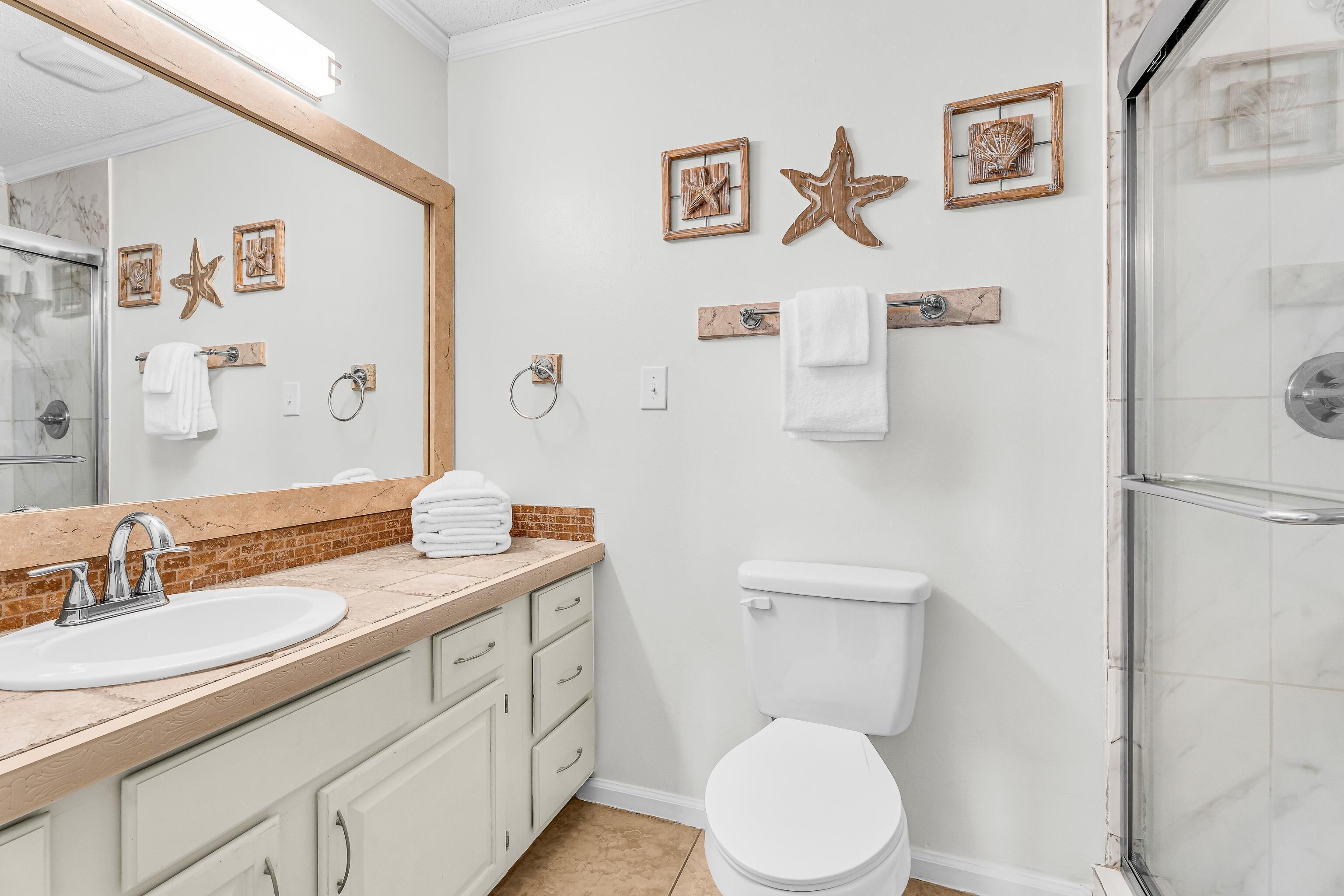 Baño con lavamanos, inodoro y ducha. Hay decoraciones de estrellas de mar en la pared y un toallero.