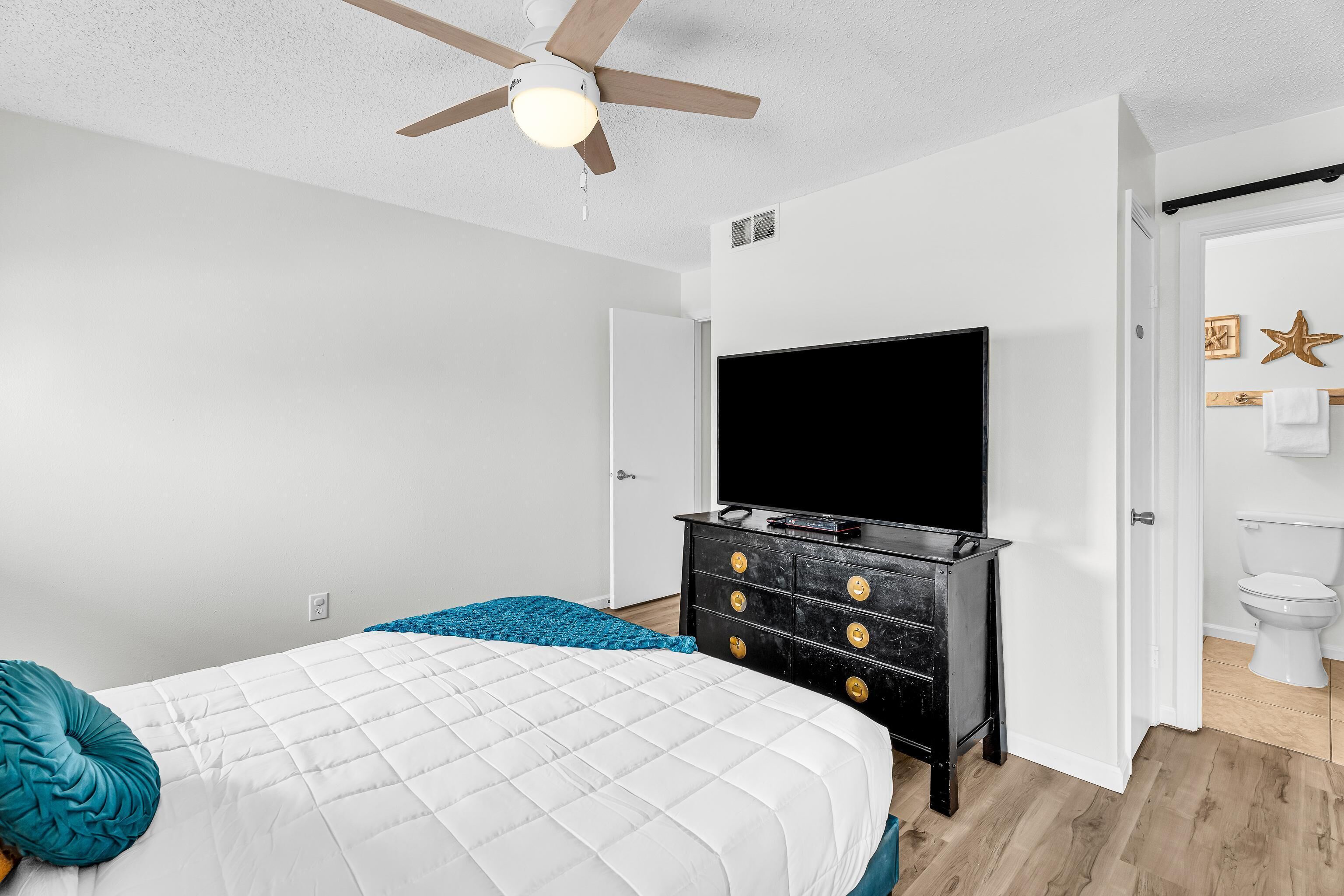 A bedroom with a bed, a dresser, a television, and a door leading to a bathroom.