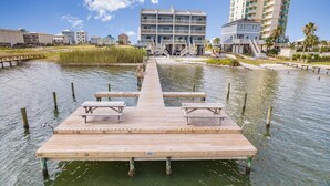 A wooden pier with picnic tables extending into a body of water, surrounded by buildings and palm trees. - Summer House West B102 (Gulf Shores)