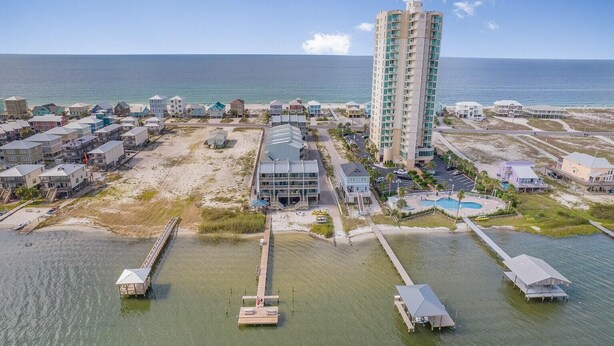 An aerial view of a coastal resort with a tall hotel, beach houses, and a pier extending into the water. - Summer House West B102 (Gulf Shores)