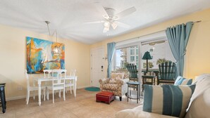 A living room with a dining table, a sofa, a ceiling fan, and a painting on the wall. - Summer House West B102 (Gulf Shores)