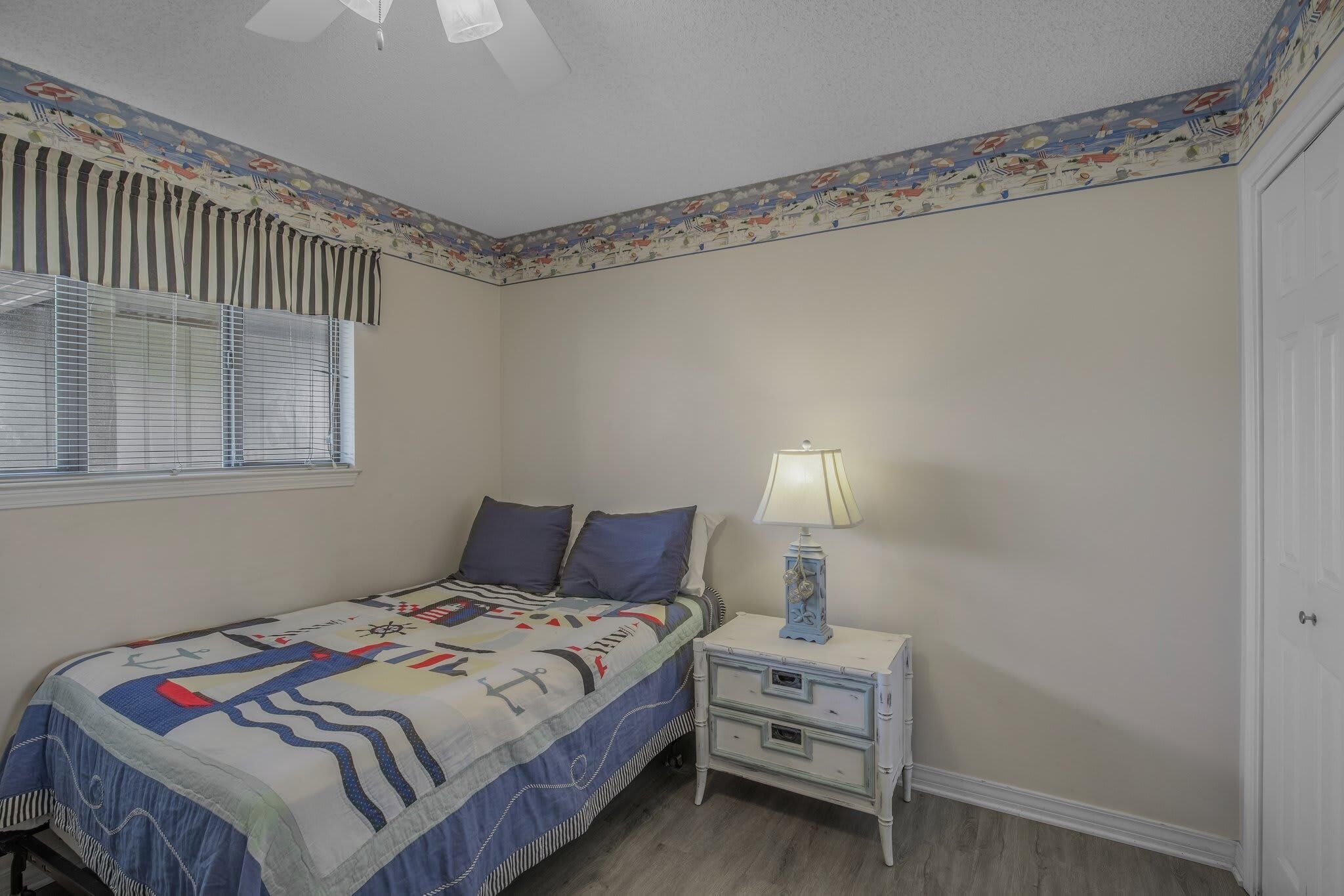 A bedroom with a bed, nightstand, lamp, and window with blinds.