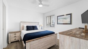 Quarto com cama, mesa de cabeceira e escrivaninha com cadeira.