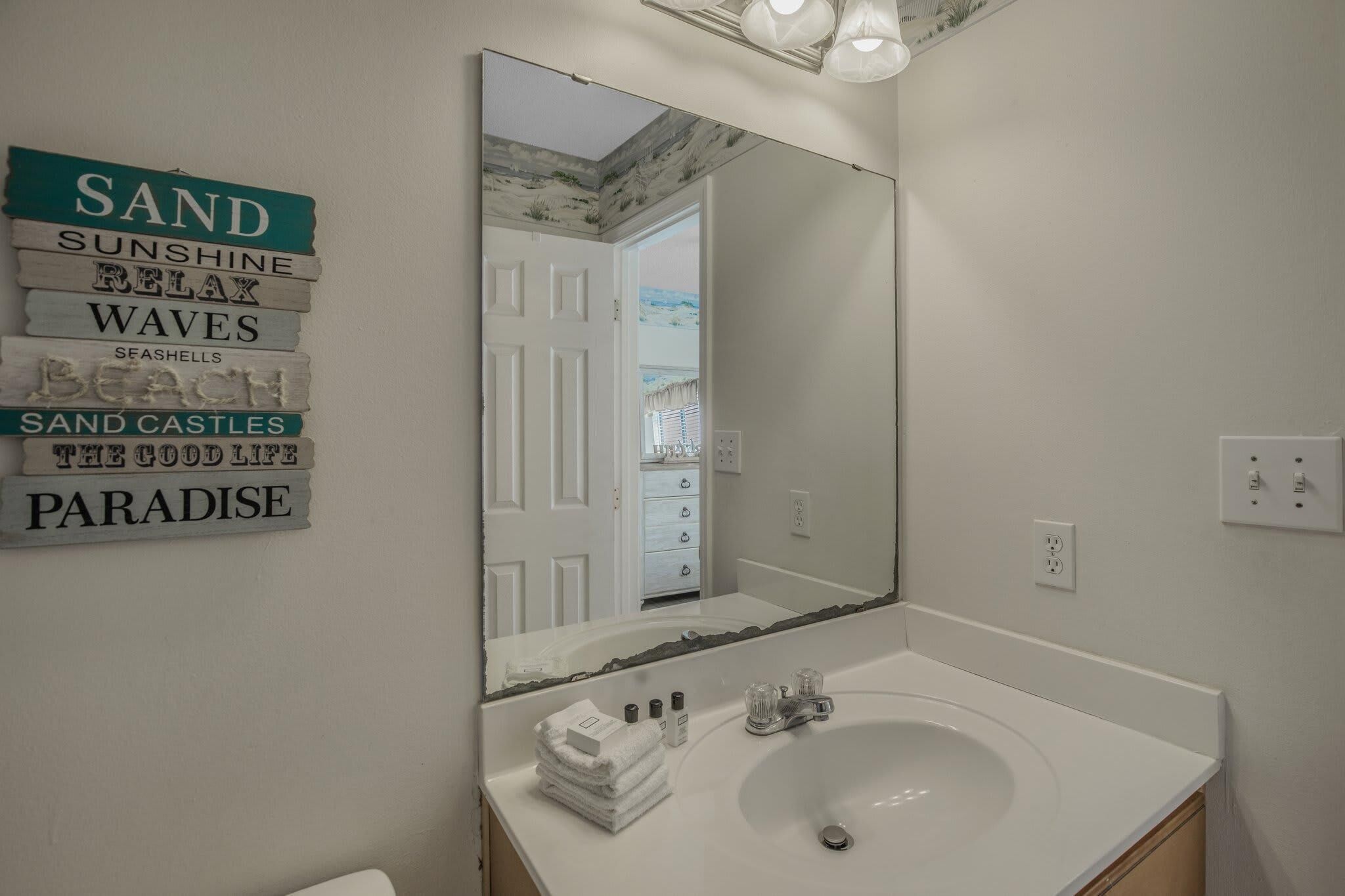 A bathroom with a large mirror, a white sink, and a towel stack.