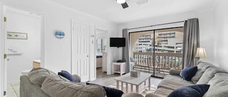 A living room with a ceiling fan, a television, and a large window with a view of buildings.